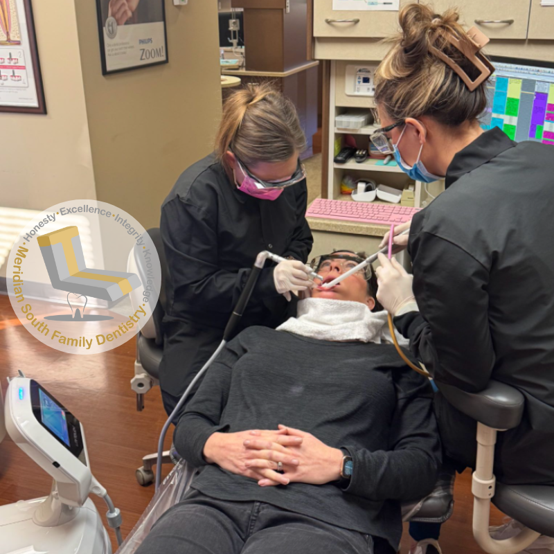 Dentists performing a dental procedure on a patient in a modern treatment room with digital equipment.